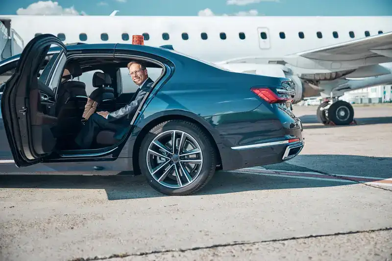 A stylish man in a tailored suit steps into a luxury black car on the airport tarmac, ready for his HOU to Galveston transfer, symbolizing executive Galveston Hobby airport transportation.